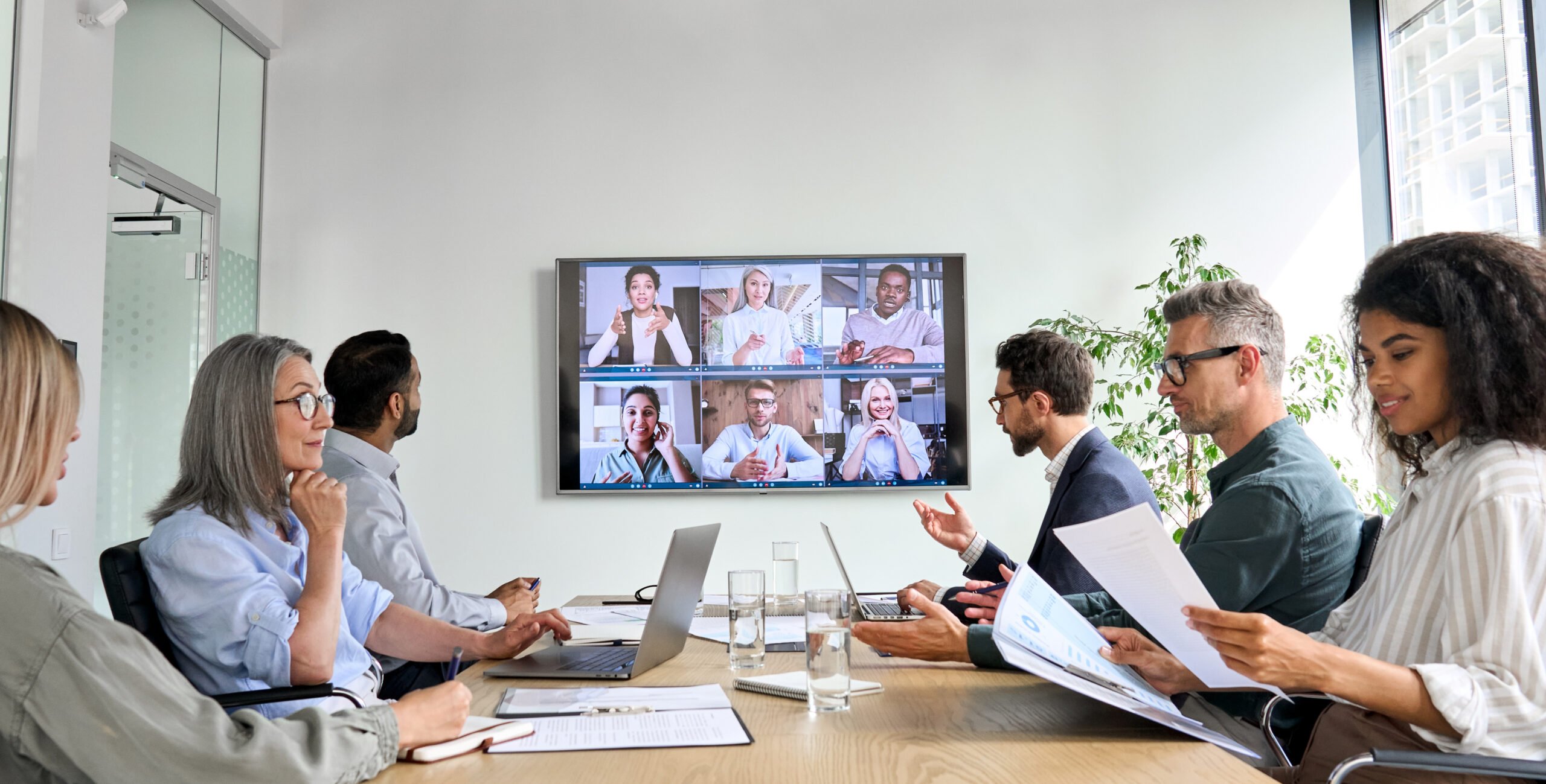 Diverse company employees having online business conference video call on tv screen monitor in board meeting room. 