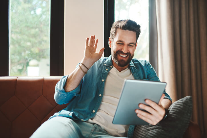 Remote worker on a video call using  his tablet while chilling on the sofa at home