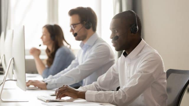 serious african call center agent in headset working on computer