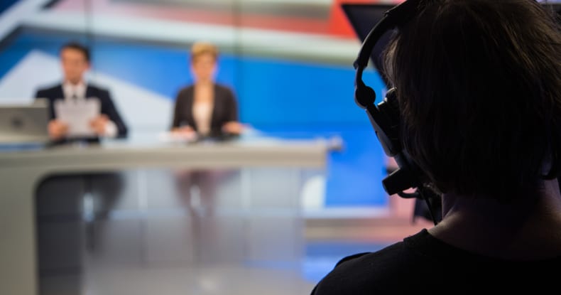 Cameraman filming news presenters in television studio.