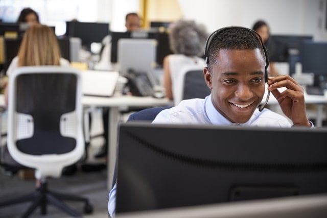 Young man working at computer with headset in busy local council office