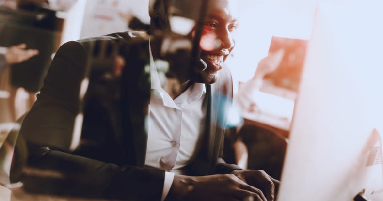 Man sitting at a desk working in a contact centre, wearing headphones and working at his computer.