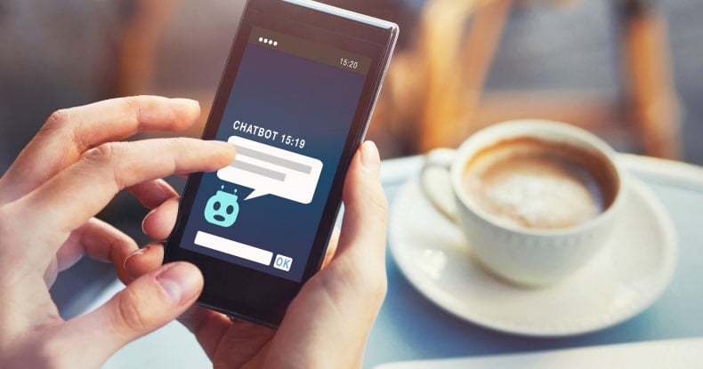 photo of someone holding a mobile phone and using an online chatbot service while they are sitting at a cafe table with a cup of coffee