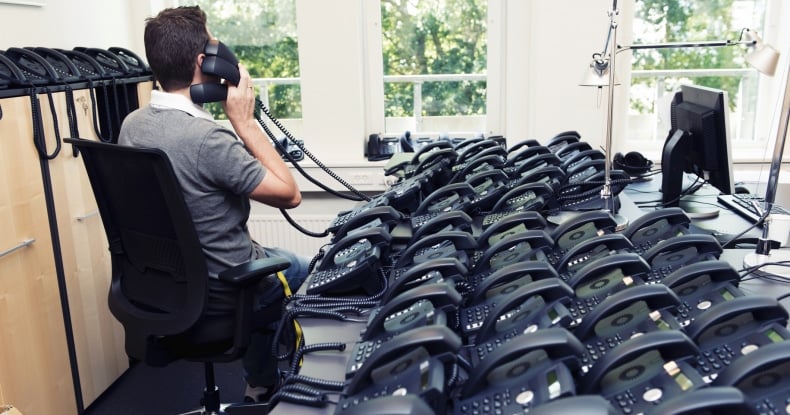 photo of Man busy answering lots of phone calls from a desk with many phones on it