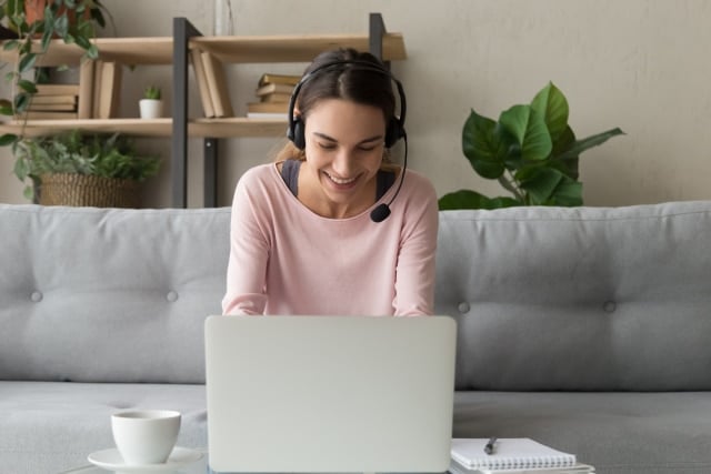 Smiling woman wear wireless headset using laptop at home making a phone call on her computer