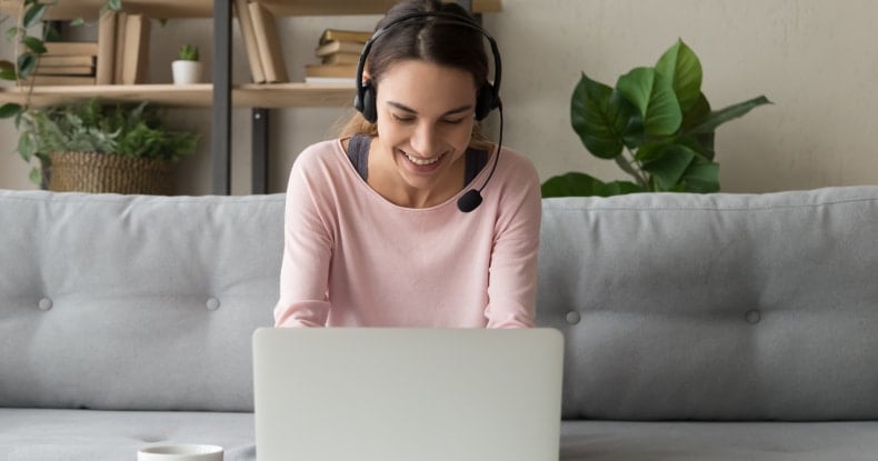 Smiling woman wear wireless headset using laptop at home making a phone call on her computer