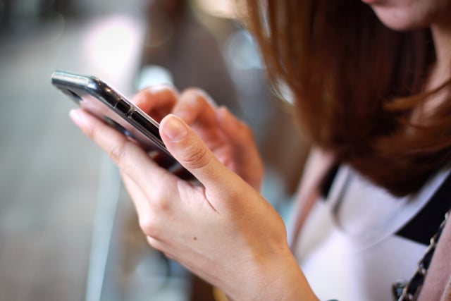 a woman holds a mobile phone in one hand and uses it with another, it's a close up photo of her hands