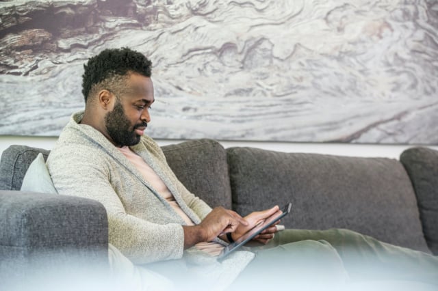 man on a grey sofa is interacting with a digital tablet while working from home