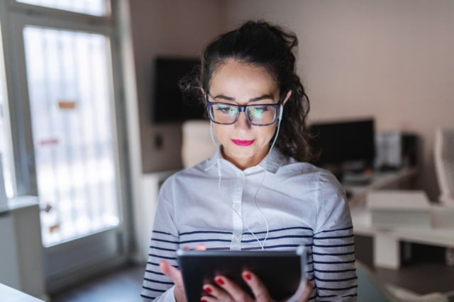 close up of beautiful caucasian woman with eyeglasses using tablet for video call earphones in ears