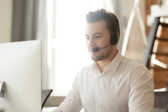 Call centre operator in headset talking with customer, using computer