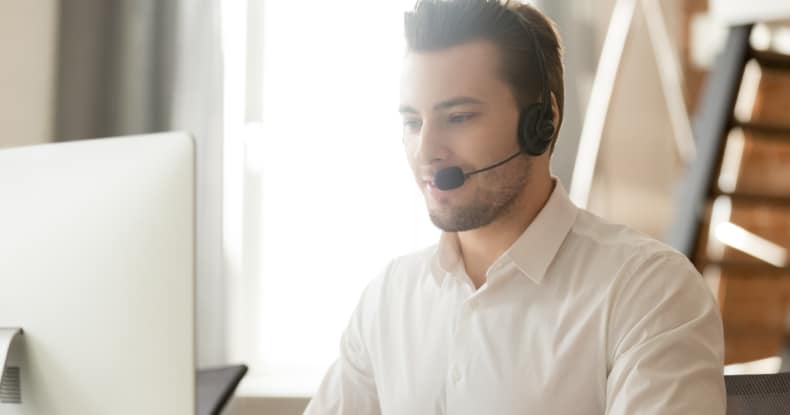 Call centre operator in headset talking with customer, using computer