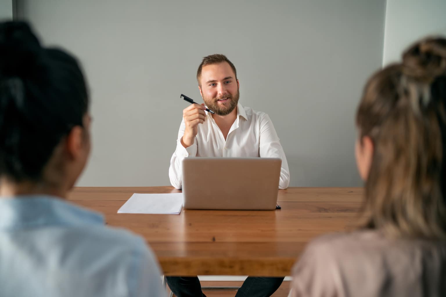 A person sitting at a table with a pen in hand while interviewing two candidates