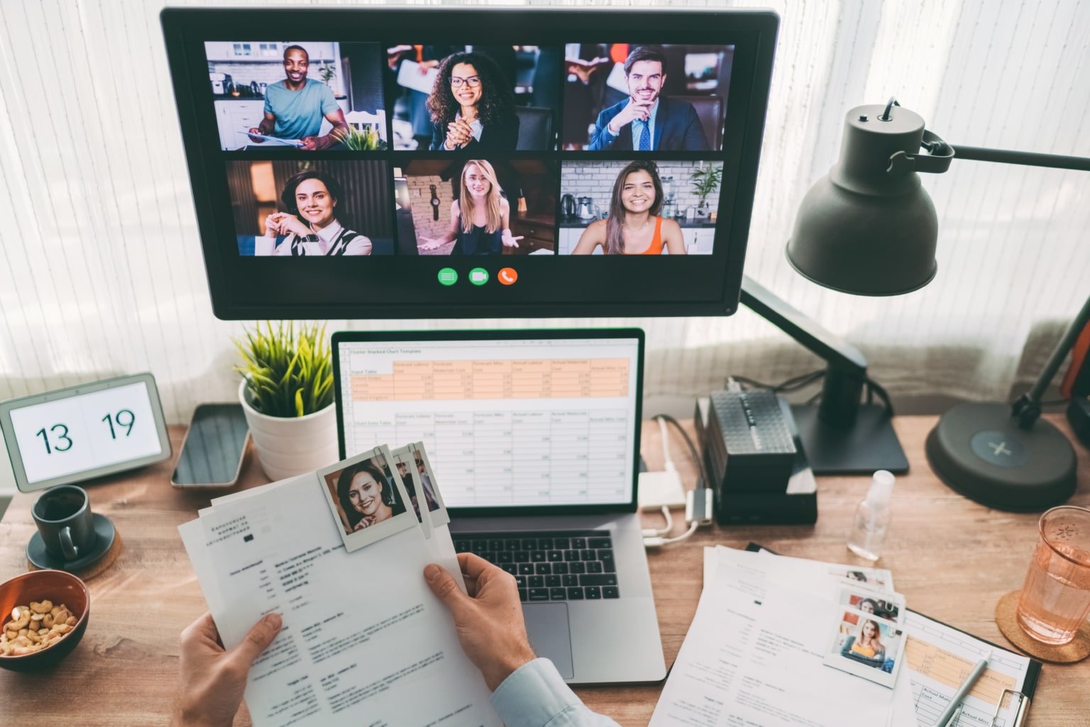 A person holding resumes while interviewing candidates on a computer