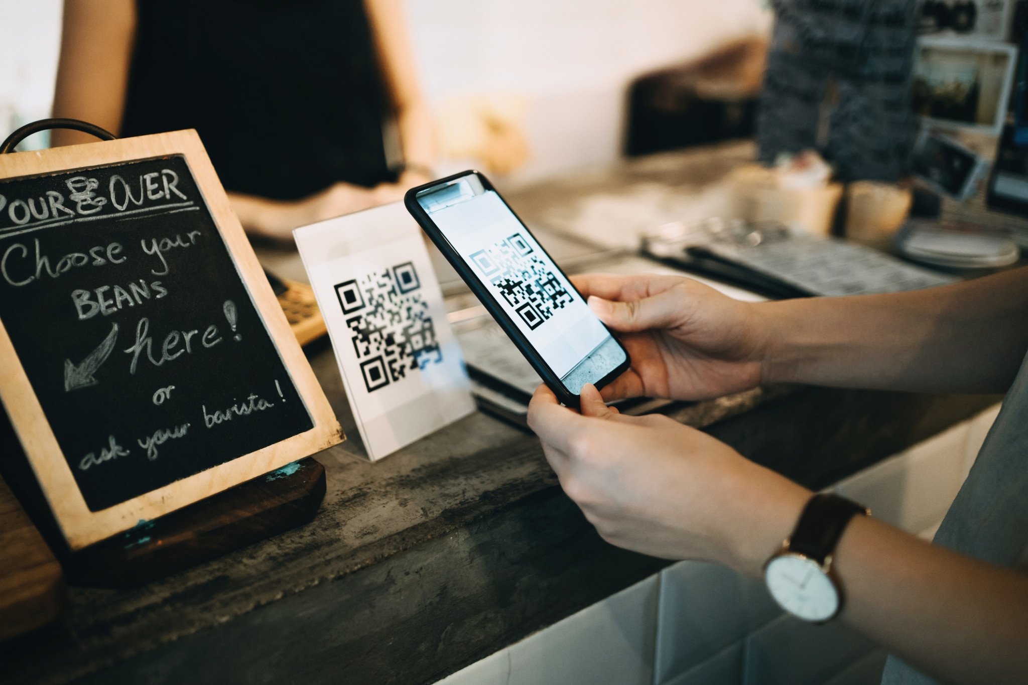 Customer scanning QR code, making a quick and easy contactless payment with her smartphone in a cafe-973