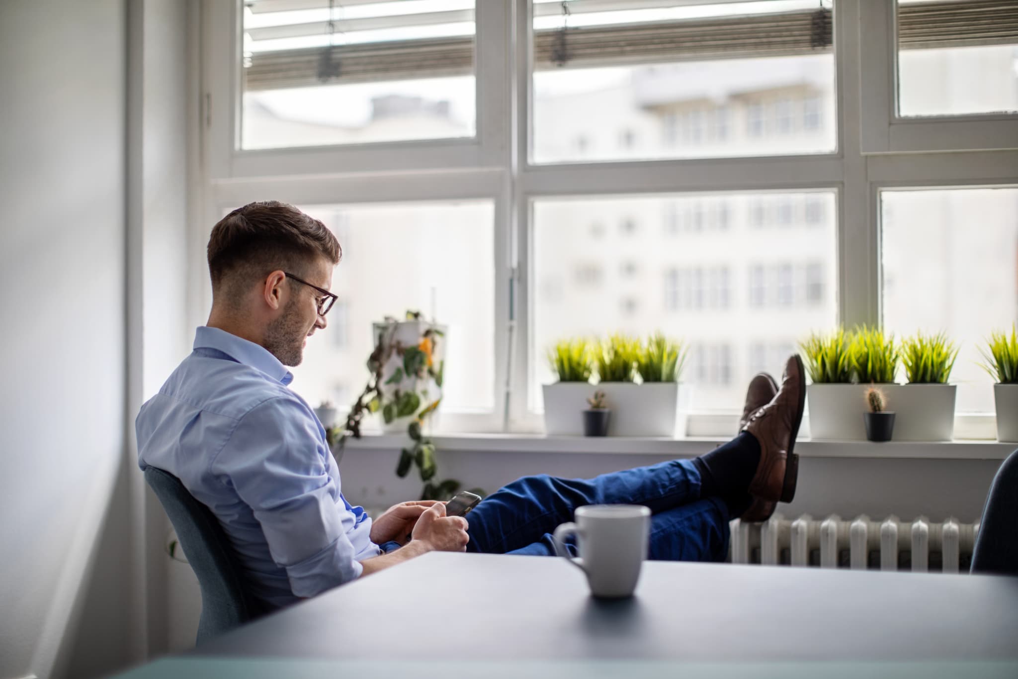 Businessman using mobile messaging app in the office with feet on the radiator