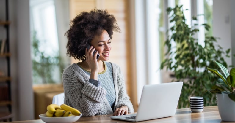 Happy black woman talking on cell phone while reading an e-mail on her laptop.-391