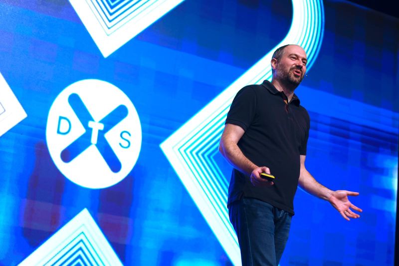 A man presenting on stage in front of an illuminated screen