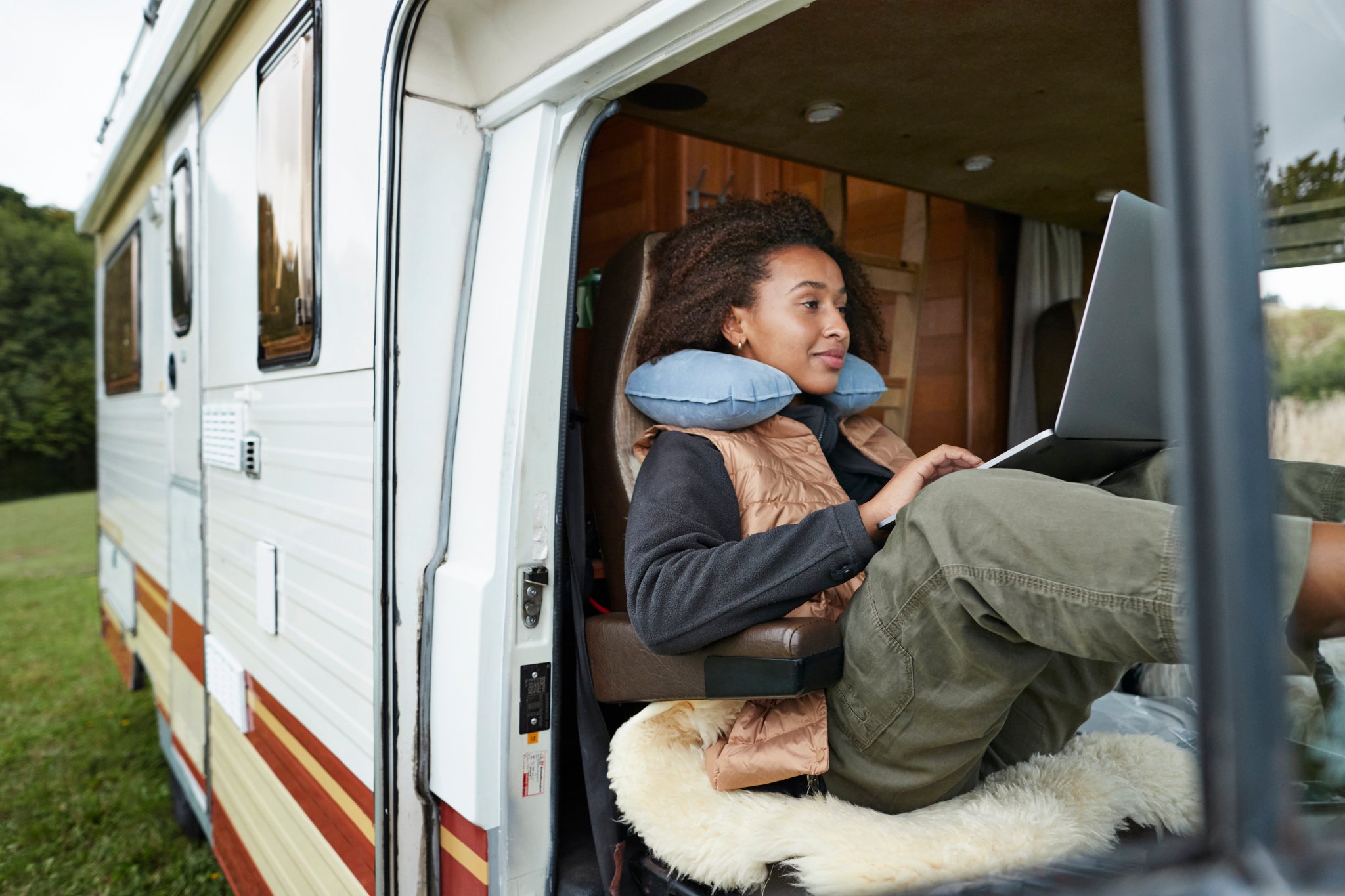 Woman with neck pillow using laptop in motor van