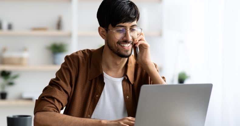 Cheerful indian guy businessman with laptop having phone conversation-406