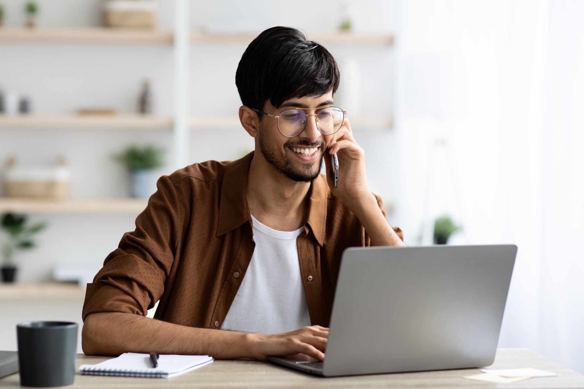 Cheerful indian guy businessman with laptop having phone conversation-363