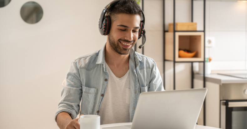 Portrait of smiling man wearing headphones with microphone using laptop at home.-817