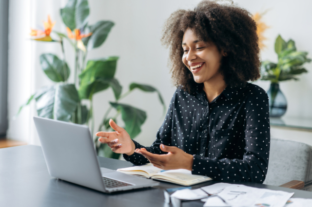 Successful positive young adult woman african woman freelancer, manager, CEO, sitting in office at laptop, talking on video call with client or employees, discussing business strategy, gesturing,smile-821