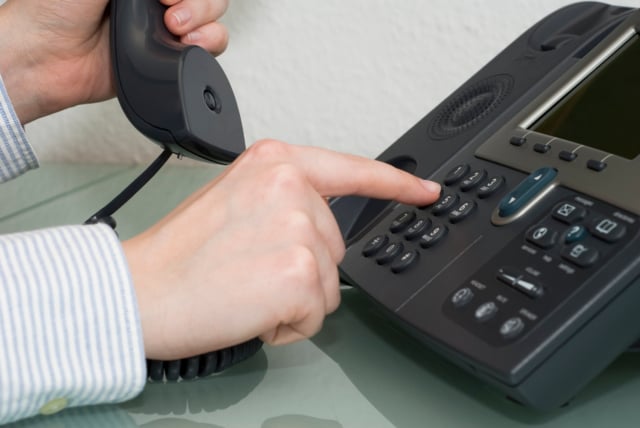 A hand dialing a number on a VoIP phone with AI elements in the background.