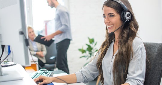 Friendly young woman call center operator with headset using computer at office