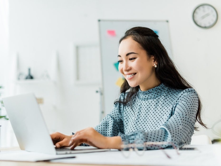 Beautiful smiling asian businesswoman sitting at desk and using laptop in office