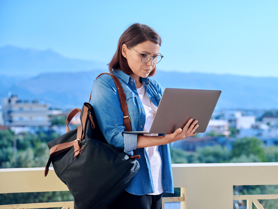 Woman outside holding a laptop and carrying a backpack