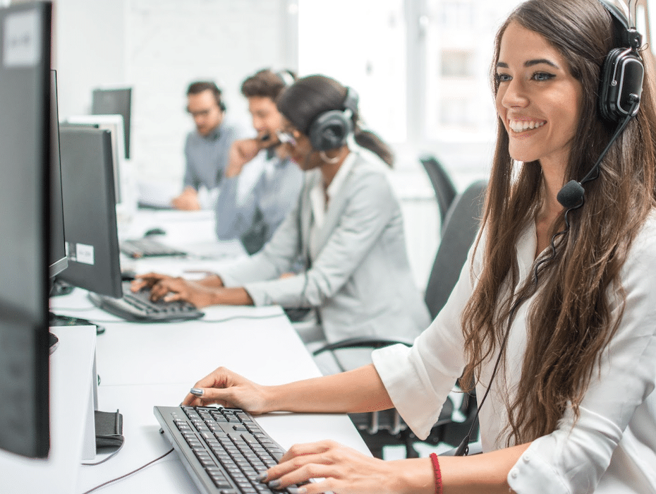 Woman with headset works on a computer with financial services colleagues in the background.