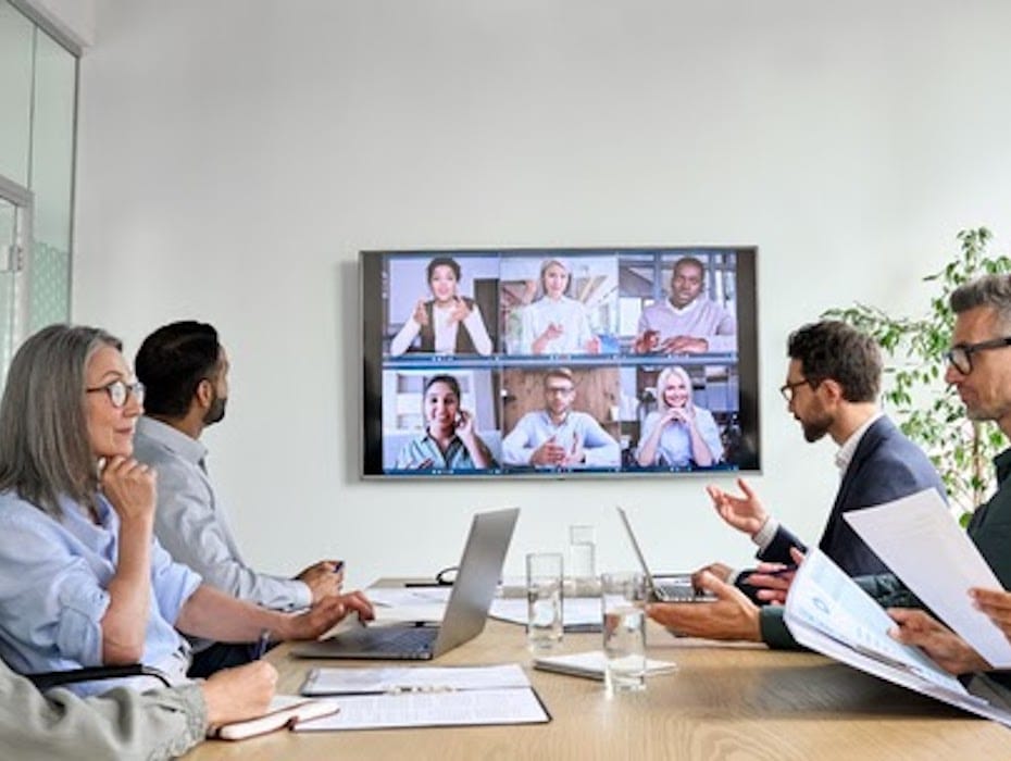 Hybrid work setup at financial services firm: Employees sitting at table and holding online meeting with remote employees