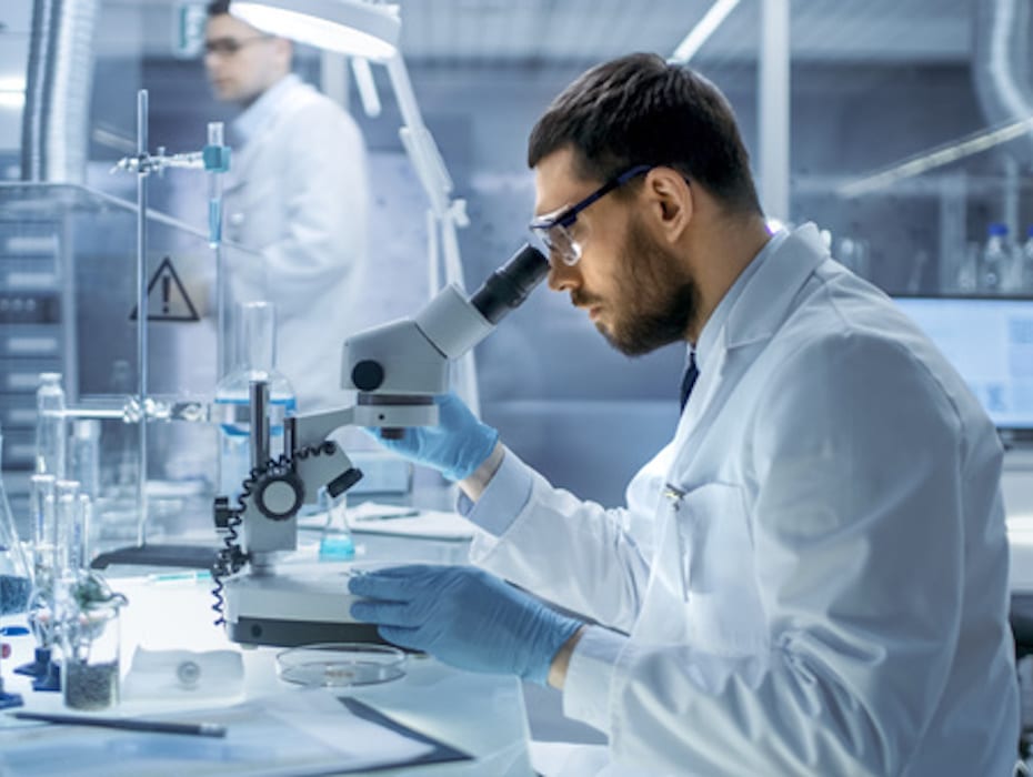 Scientist looking through a microscope in a lab setting.