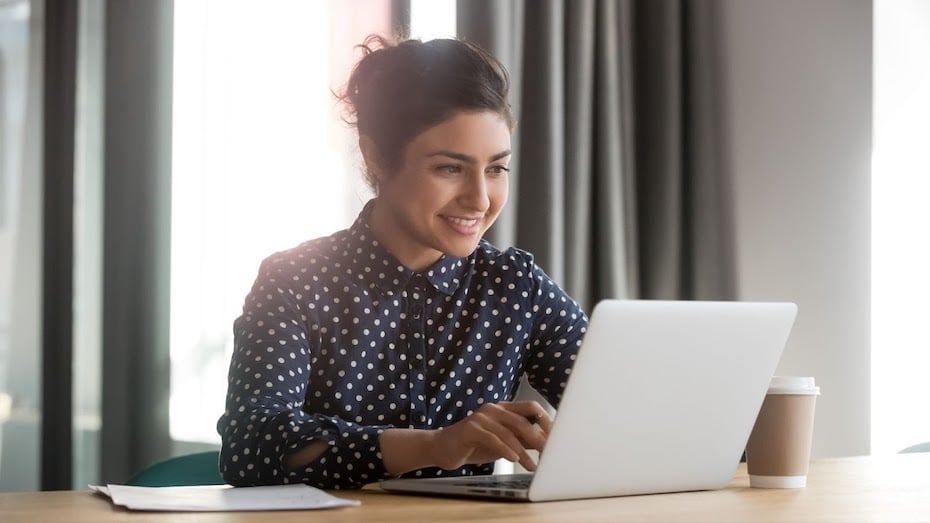 Smiling student typing on laptop while connecting with classmates online.