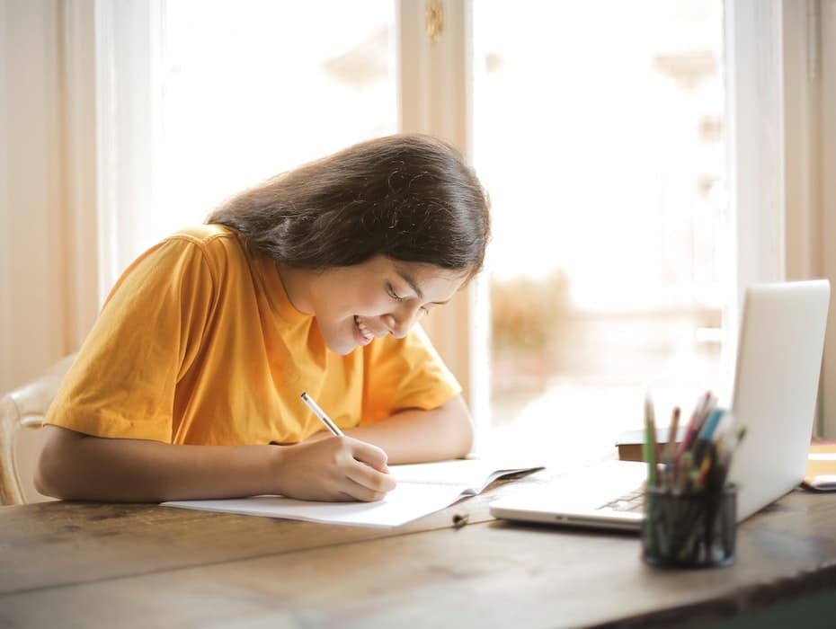 A smiling student doing homework at her desk.