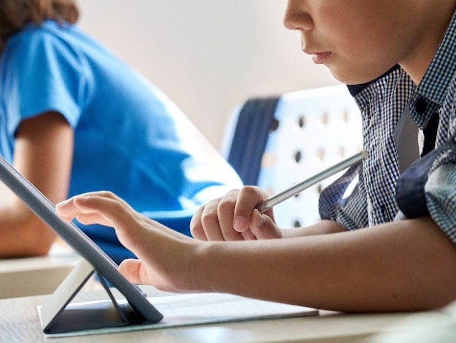 Side profile view of student sitting at desk learning from a tablet