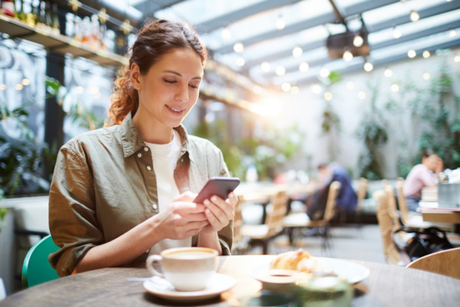 A woman sitting at a table using her mobile phone to handle insurance communications