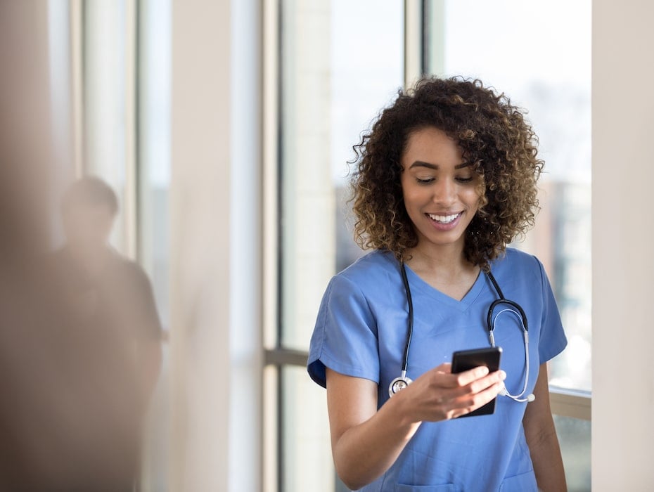 Attractive young female nurse or doctor checks messages on smartphone as she walks in a hospital hallway.