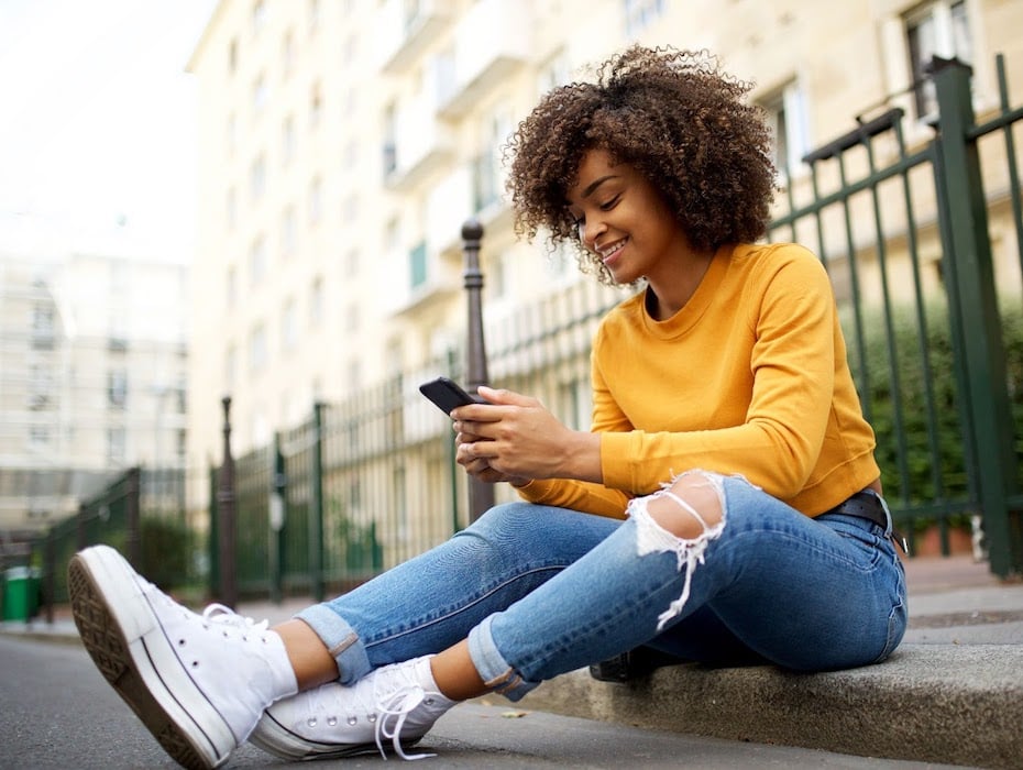 A woman sits on the sidewalk using her mobile phone