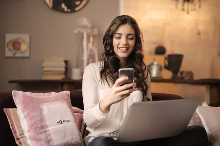 A woman uses her mobile phone while sitting on her bed.