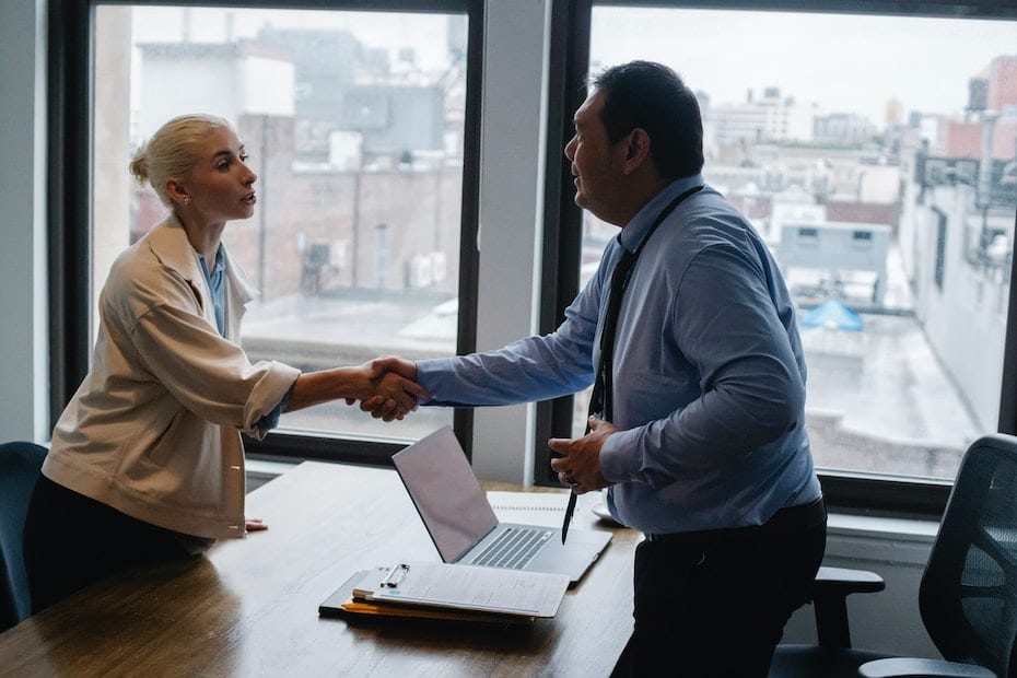 Two government agency employees shaking hands over a desk.