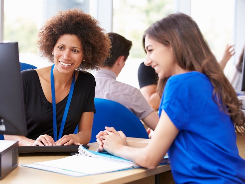 Higher Ed administrator and student look at a computer screen together while smiling