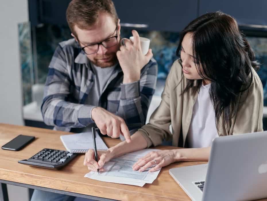 Two credit union clients sit at table using laptop and mobile phone.