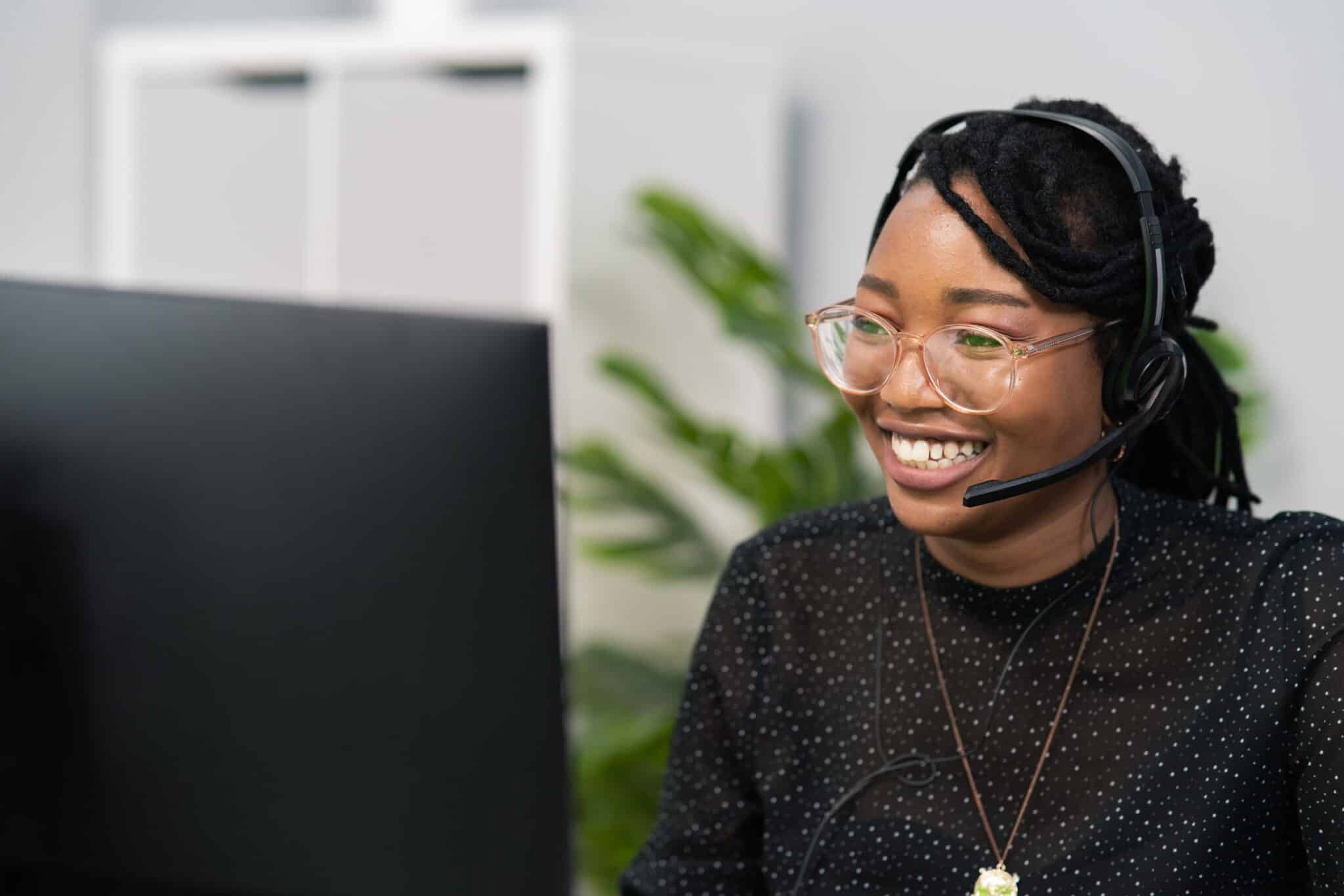 Customer service agent, financial advisor call center employee sits at desk in company in front of computer screen, headphones with microphone on ears, connecting with caller, solving problem